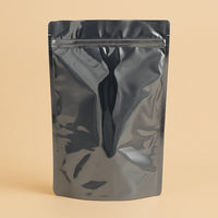 Glossy black sachet pouch with a resealable zipper, shown standing upright against a beige background.