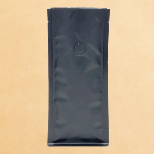 Black flat bottom coffee pouch with one-way valve, displayed upright against a beige background.