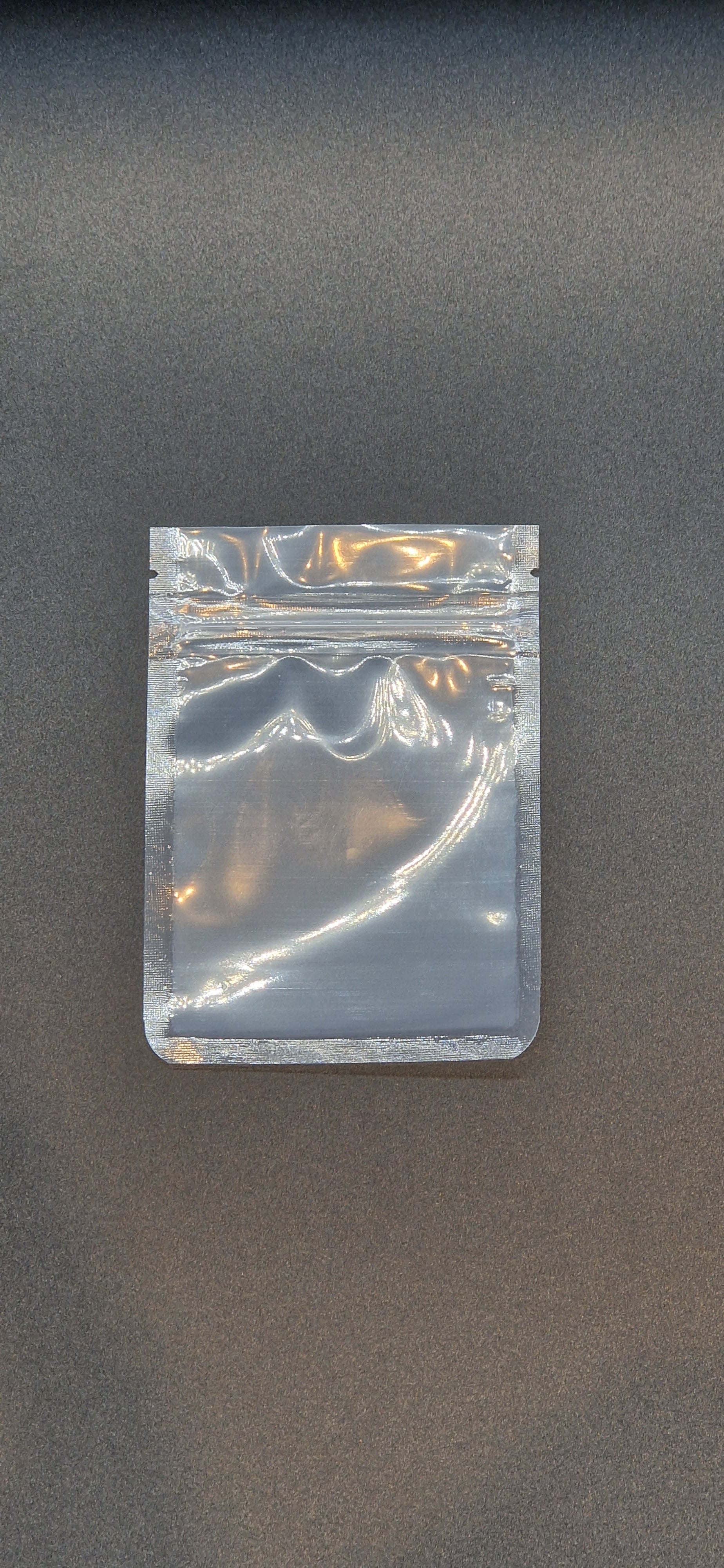 Clear resealable sachet pouch with a press-to-close seal, displayed flat and empty against a dark grey background.