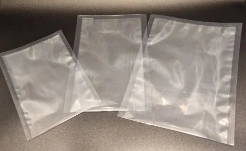3 various sized clear 3 side seal open bottom  pouches lying flat on a surface.