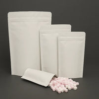 Four white kraft resealable stand up pouches in various sizes, displayed upright and partially filled with pink and white sweets, set against a dark background.