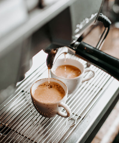 Espresso being poured from a machine into two cups.