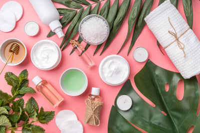 Cosmetic products and green leaves on a pink background