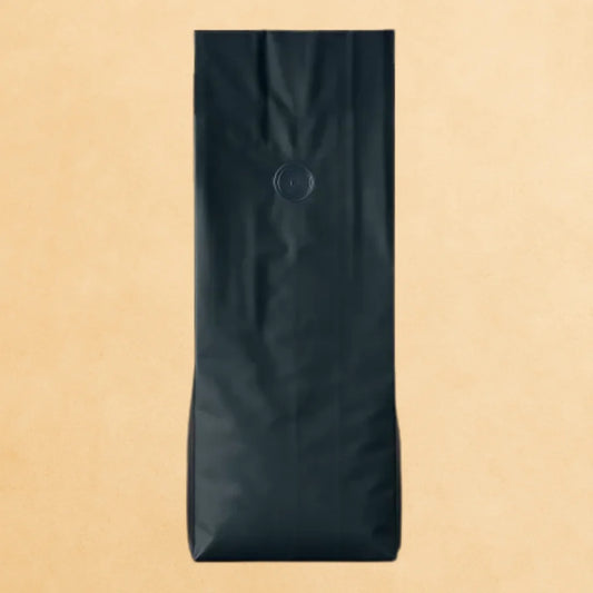 Matt black side gusset coffee bag with one-way valve and open top, displayed upright against a beige background.