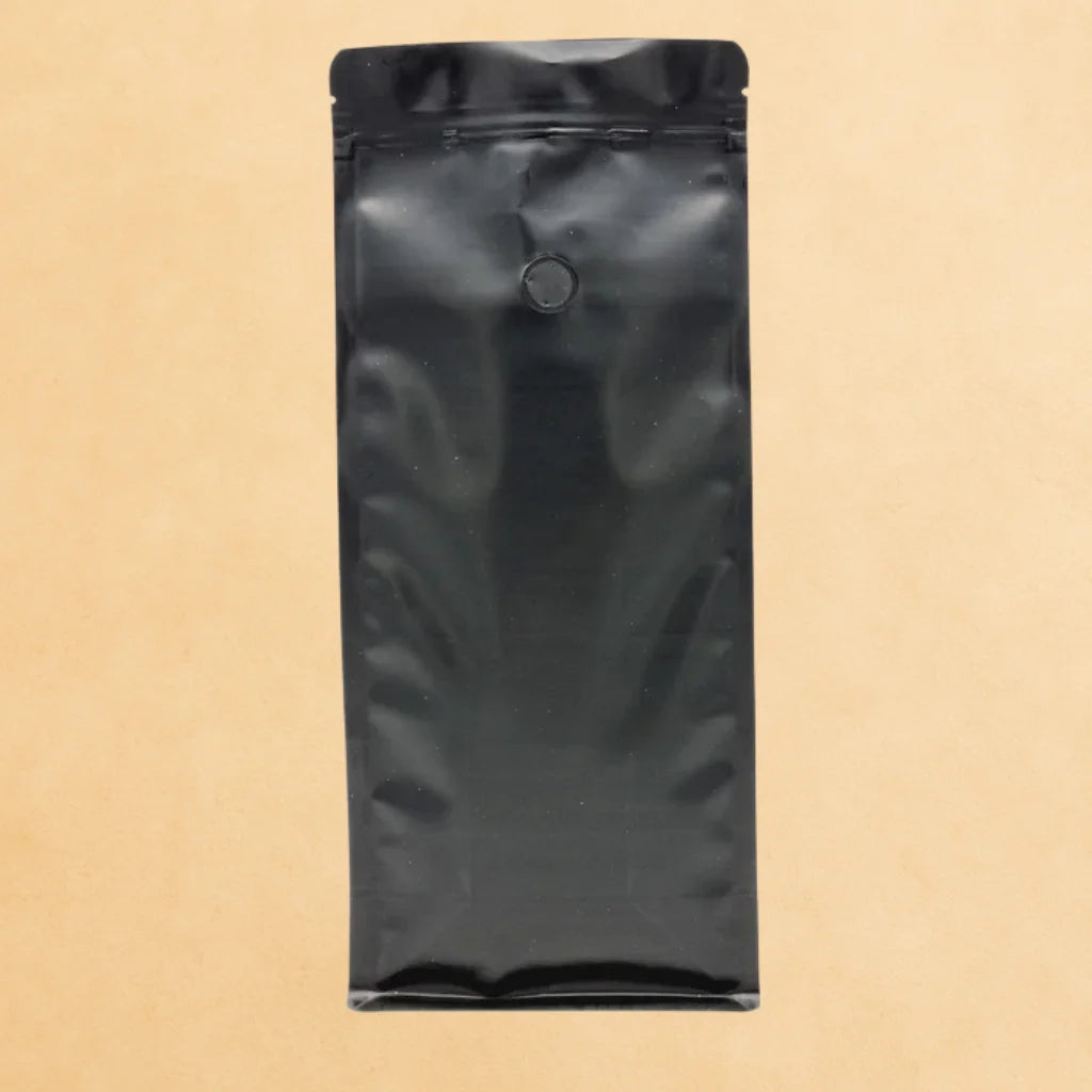 Black flat bottom side gusset coffee pouch with valve and resealable zipper, made from Code 4 recyclable material, displayed upright against a beige background.