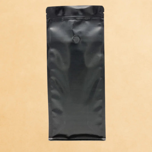 Black flat bottom side gusset coffee pouch with valve and resealable zipper, made from Code 4 recyclable material, displayed upright against a beige background.