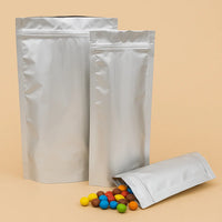 Foil resealable stand up pouches in various sizes, with one pouch open and spilling colourful coated sweets, displayed against a beige background.