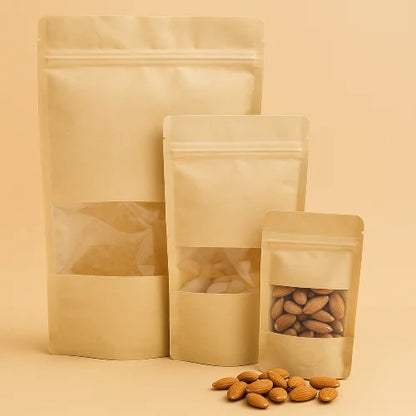 Three brown kraft pouches with clear window panels on a beige background, with almonds spilling out.