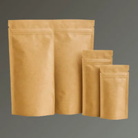 Four brown kraft compostable resealable stand up pouches in different sizes, displayed upright against a dark background.