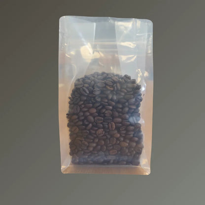 Clear recyclable flat bottom bag with Rip n Zip and open top, filled with coffee beans, shown upright against a grey background.