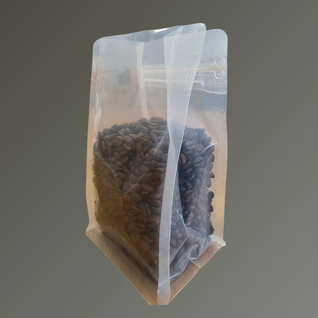 Clear recyclable flat bottom bag with Rip n Zip and open top, filled with coffee beans, shown from a side angle against a grey background.