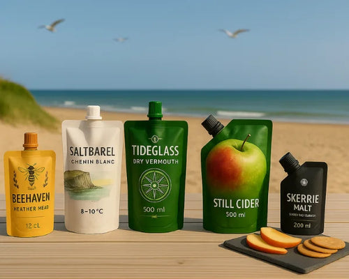 5 spout pouches on a table by the beach containing alcoholic drinks.