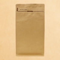 Flat bottom kraft coffee bag with Rip n Zip opening and one-way valve, displayed upright against a beige background.