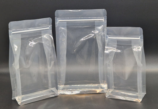 Three clear resealable box bottom bags in different sizes, displayed empty and upright against a black background.