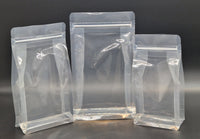 Three clear resealable box bottom bags in different sizes, displayed empty and upright against a black background.