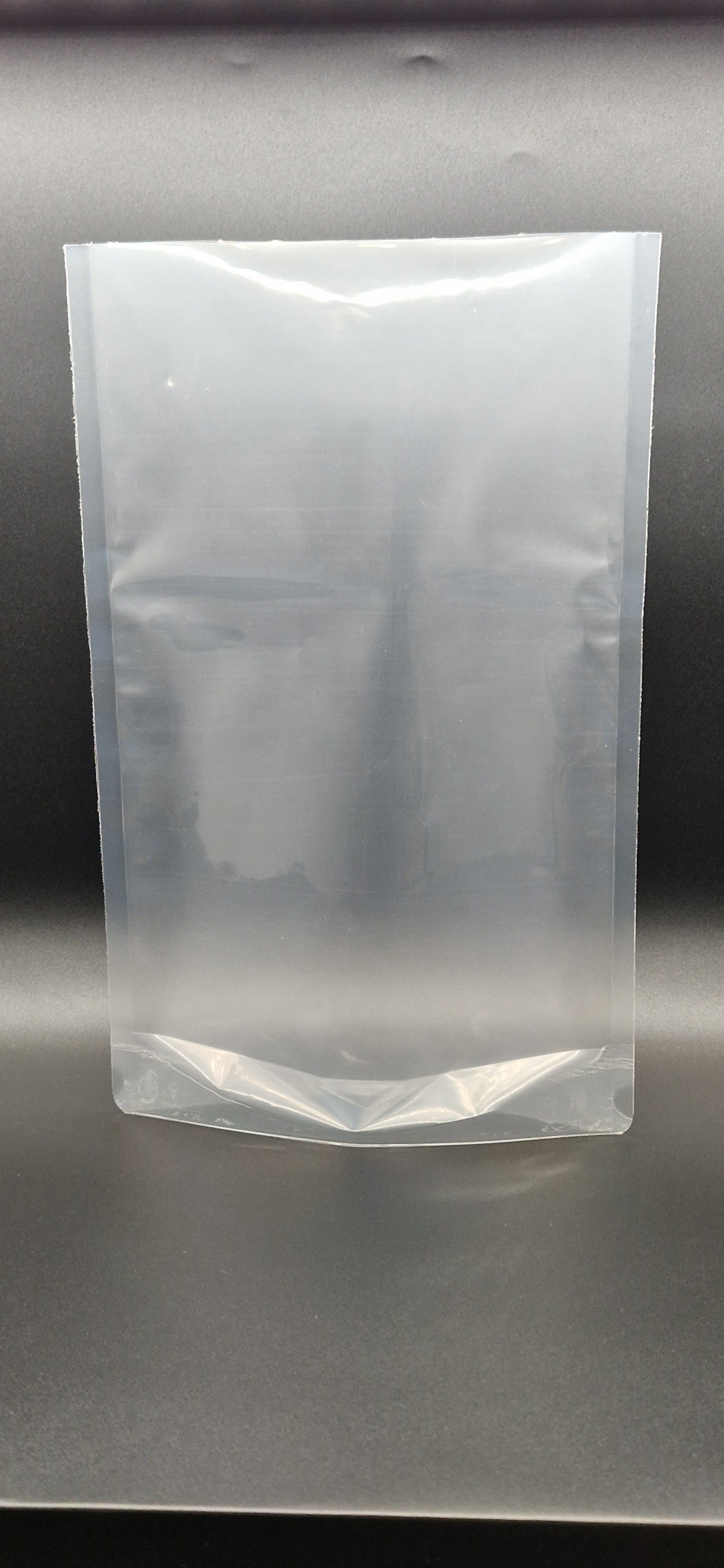 Clear open top stand up pouch displayed upright against a dark background, shown empty and unsealed.