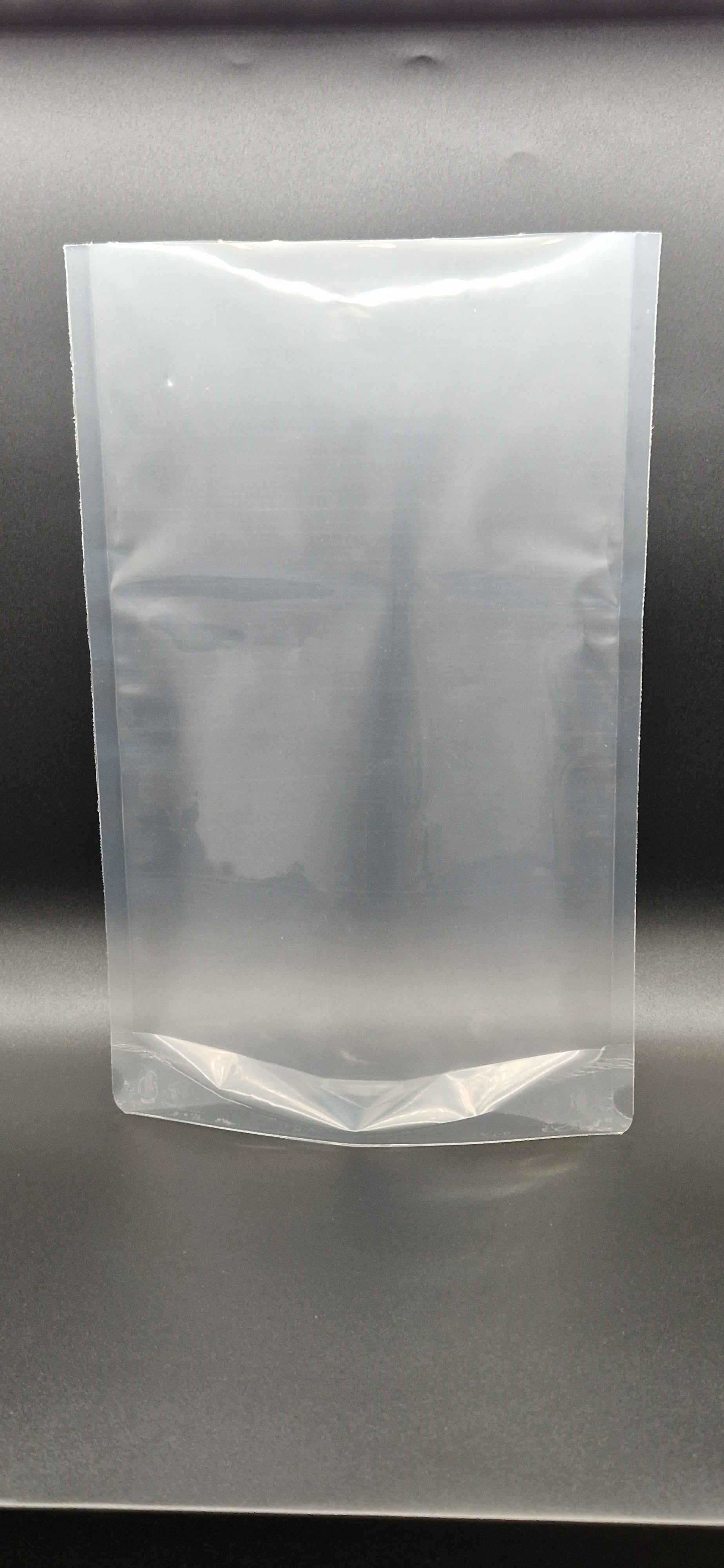 Clear open top stand up pouch displayed upright against a dark background, shown empty and unsealed.