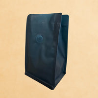 Side view of a green recyclable flat bottom coffee bag with one-way valve, rip n zip closure, and open top, shown standing upright against a neutral background.