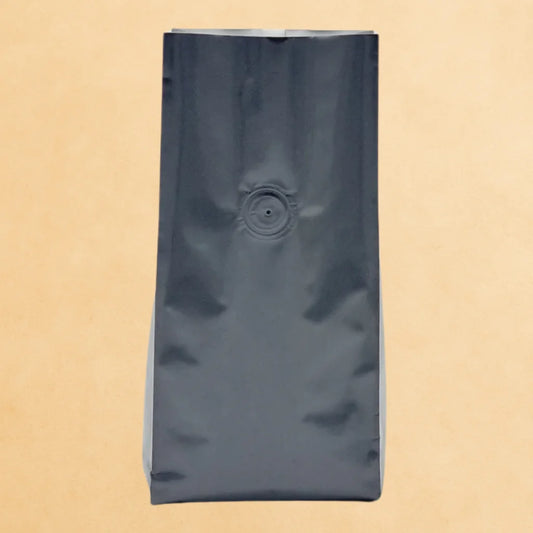 Matt black open top flat bottom coffee pouch with valve, shown upright against a beige background.